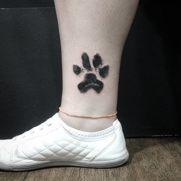 Dog paw print tattoo on the ankle above a white shoe, showcasing pawesome design.