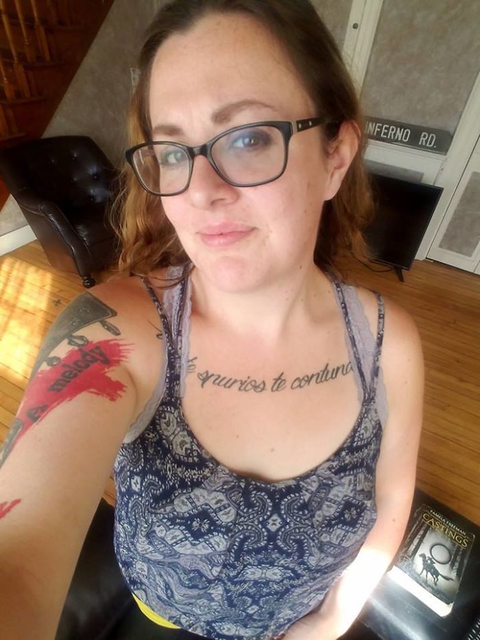 Woman with tattoos, glasses, and a patterned top smiling in a casual setting, illustrating unseen depression symptoms.