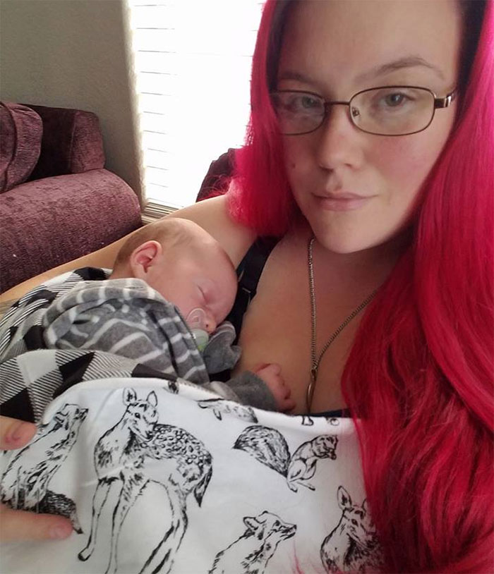 A woman with bright red hair and glasses holds a sleeping baby wrapped in a patterned blanket, illustrating depression symptoms.