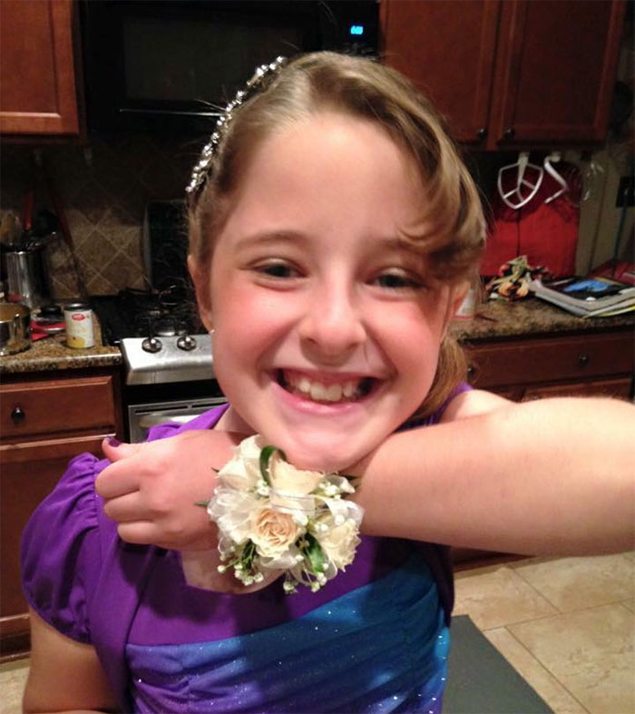 Smiling child in a purple dress holding a flower corsage, illustrating how depression symptoms have no face.