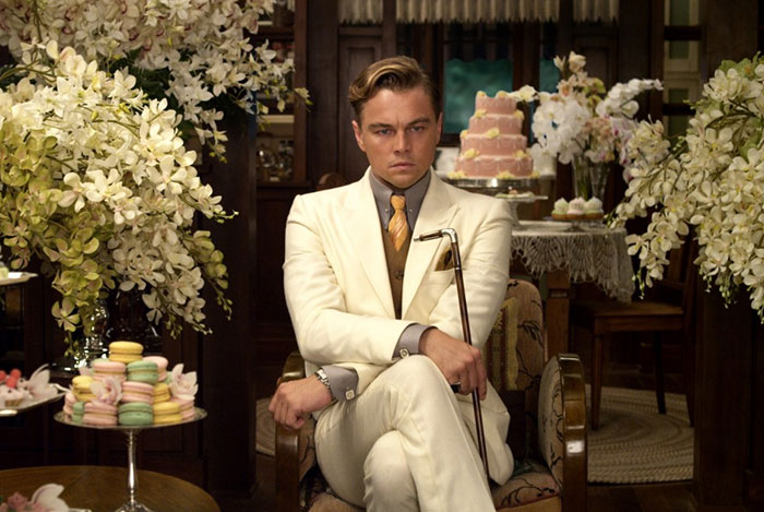 Leonardo DiCaprio in The Great Gatsby movie scene, dressed in a white suit, surrounded by flowers and desserts, movie fun facts.