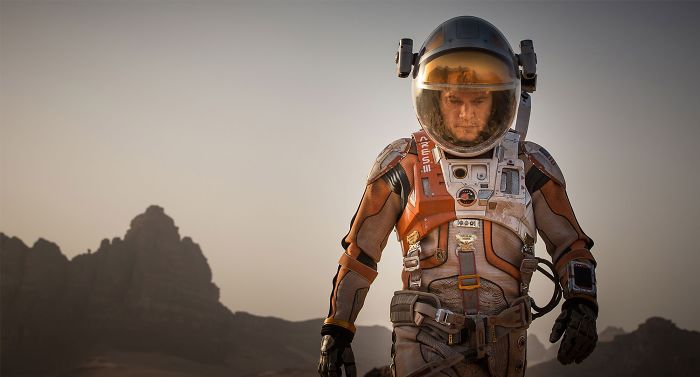 Scene from The Martian movie showing an astronaut in a detailed space suit walking on a rocky Mars surface.