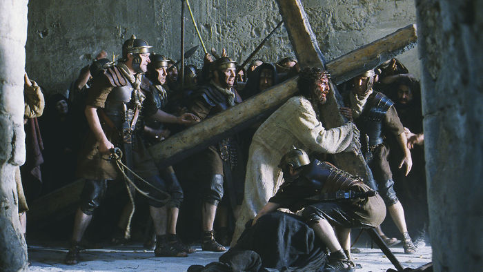 Scene from The Passion Of The Christ movie showing Jesus carrying a cross surrounded by Roman soldiers, related to fun facts about movies.