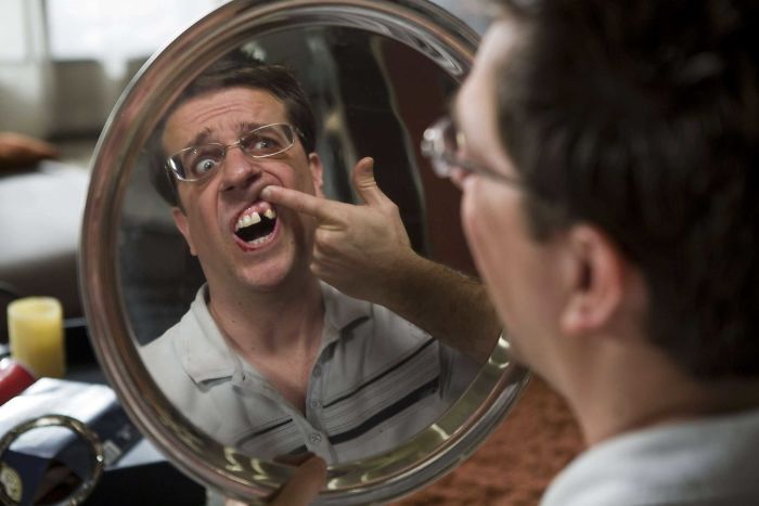 Man in a comedic movie scene from The Hangover, examining a missing tooth in a round mirror, showcasing movie fun facts.