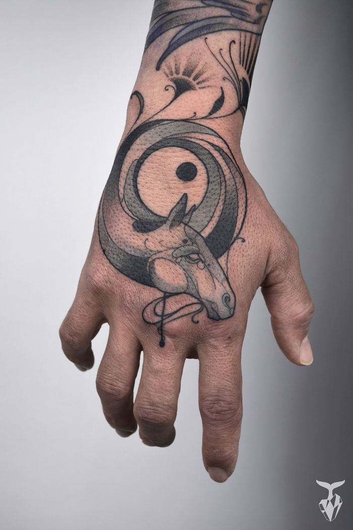 Hand with Art Nouveau-inspired tattoo featuring abstract horse and nature motifs.