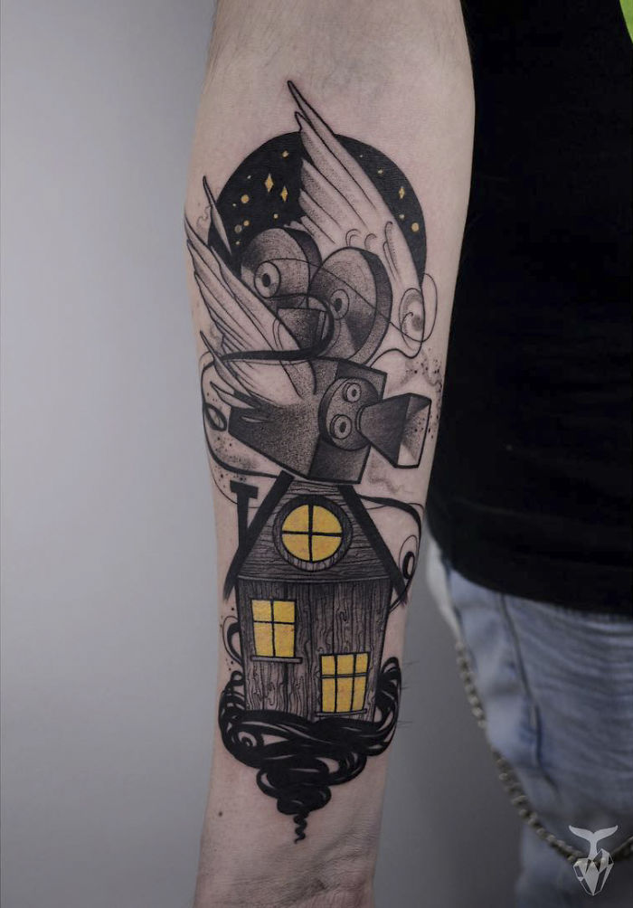 Nature and Art Nouveau inspired tattoo of a house with yellow windows and swirling designs on an arm.