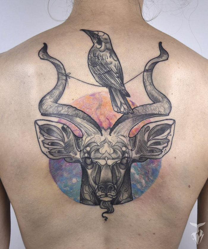 Nature and Art Nouveau inspired tattoo with a detailed design of a crow and antelope on a person's back.