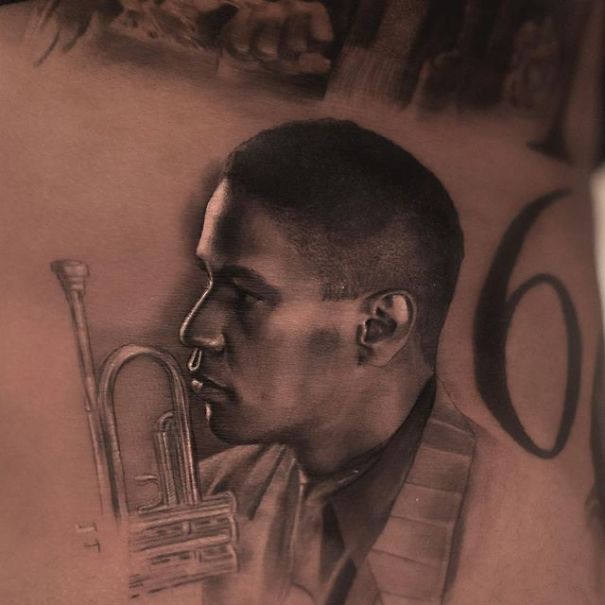 Realistic tattoo by Belgian artist of a man with a trumpet, giving a printed-on-skin illusion.