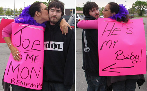 Woman holding funny airport pickup signs saying "Joe is me, Mom" and "He's my baby" while hugging a man.