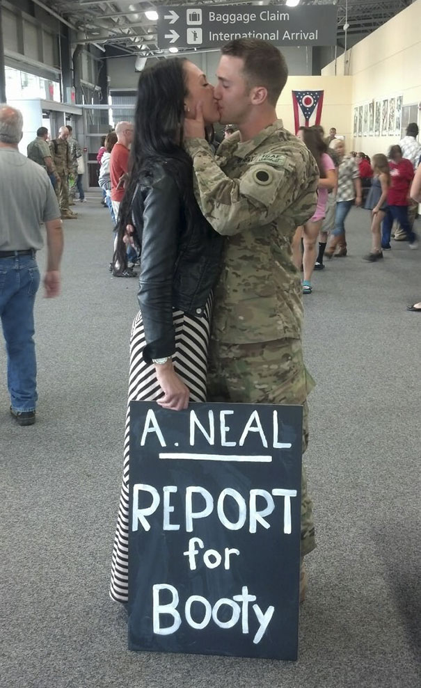 Military man and woman kissing at airport with funny pickup sign saying "Report for Booty."