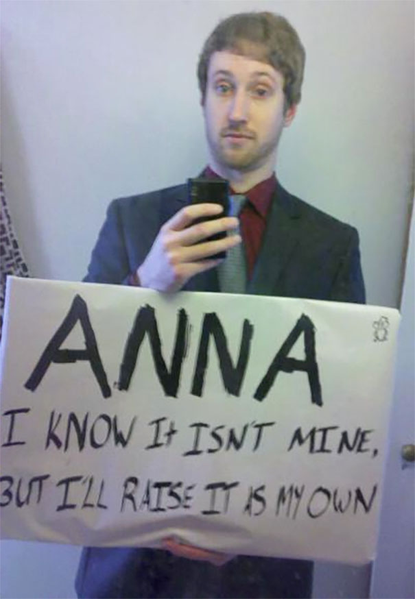 Man in a suit holding a funny airport pickup sign for Anna in a bathroom mirror selfie.