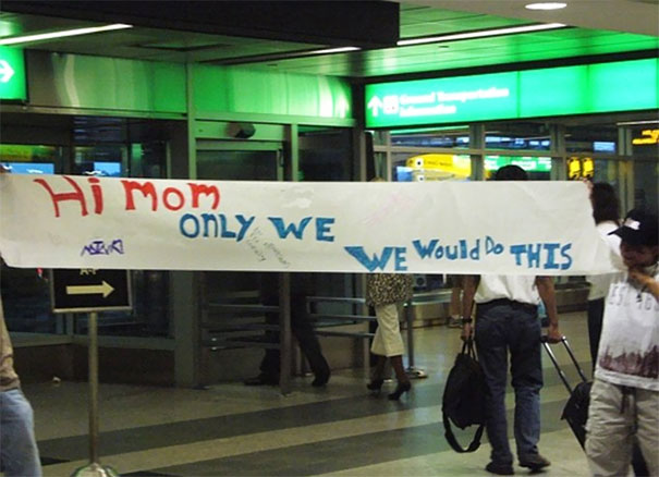 Funny airport pickup sign reading "Hi mom, only we would do this" in a busy terminal.