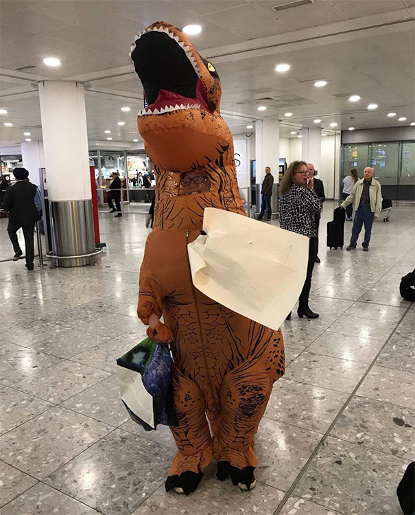 Funny airport pickup with person in dinosaur costume holding signs, amusing travelers.