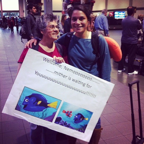 Two people holding a funny airport pickup sign referencing "Finding Nemo" at the arrivals area.