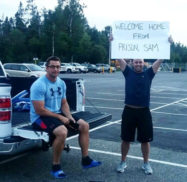 Funny airport pickup sign saying "Welcome home from prison, Sam" in parking lot.