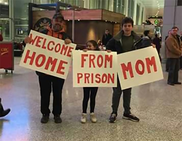 Family holding funny airport pickup signs saying "Welcome Home From Prison Mom."
