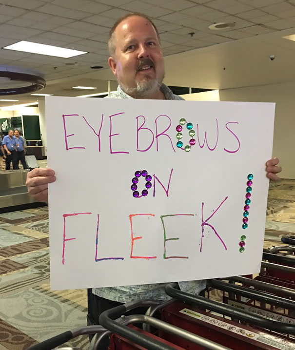 Man holding a funny airport pickup sign decorated with colorful jewels.