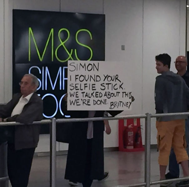 Humorous airport pickup sign held by a person, referencing a selfie stick mishap.