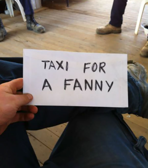 Funny airport pickup sign reading "Taxi for a F***y" held by a person sitting on a wooden floor.