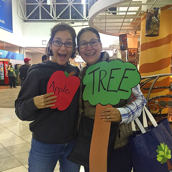 Two women with funny airport pickup signs shaped like an apple and tree.