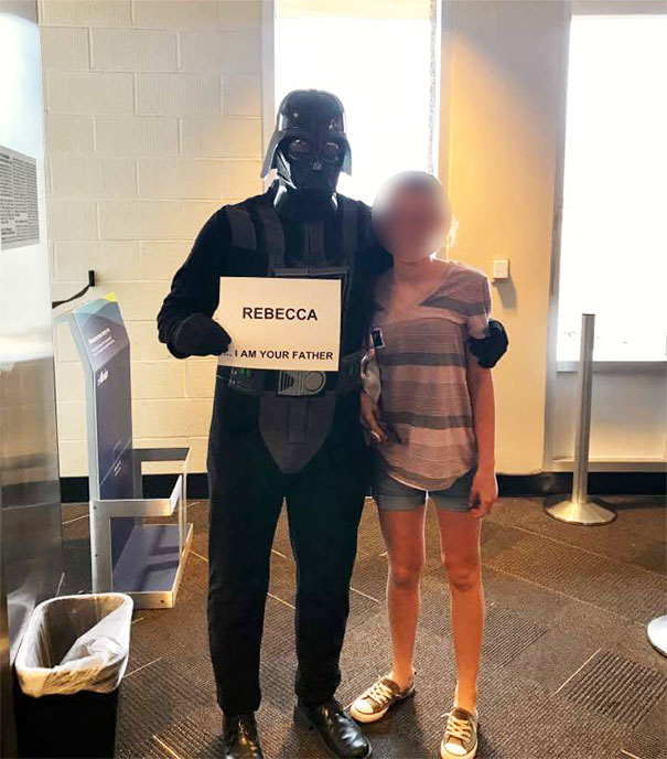 Man in costume holding a funny airport pickup sign saying “Rebecca, I am your father,” posing with a girl at the airport.