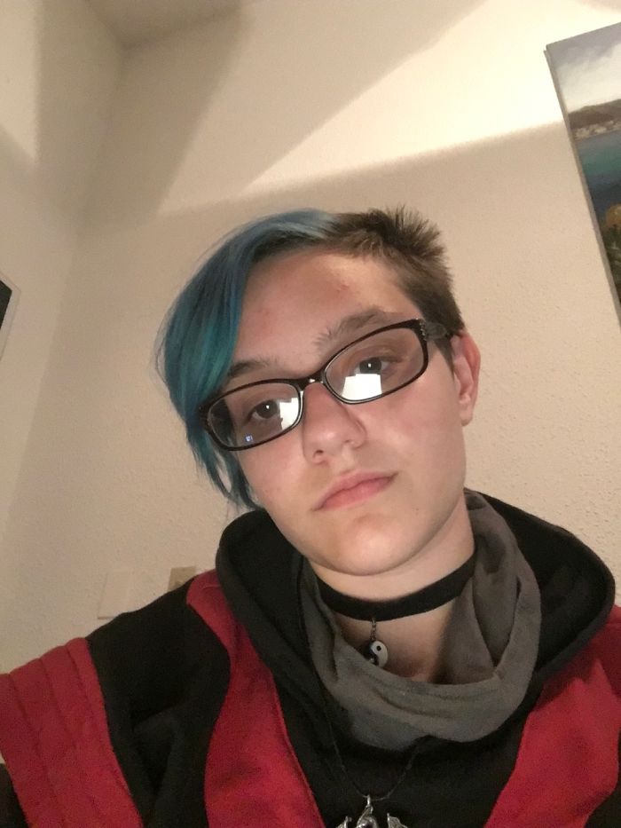 Person with blue hair and glasses showcasing that depression symptoms have no face, wearing casual attire indoors.