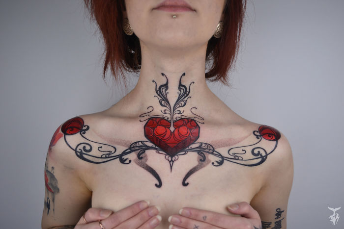 Nature and Art Nouveau inspired tattoo featuring a red heart and intricate black swirls on a woman's chest.