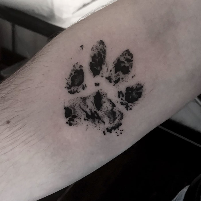 Dog paw print tattoo on inner forearm, showcasing bold black ink design.