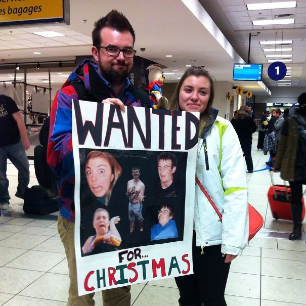 Two people at airport with a funny pickup sign featuring photos and the text "Wanted for Christmas."