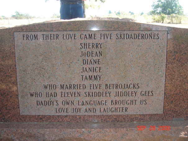 Humorous tombstone inscription listing family members and playful nicknames on a granite grave marker outdoors.