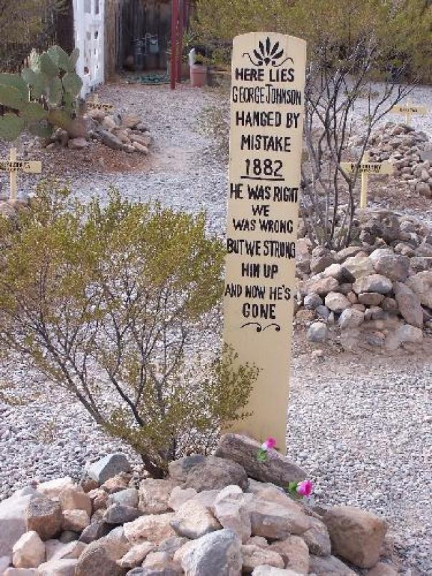 Tall humorous tombstone in a desert graveyard with a funny epitaph and rocks at the base, showcasing undying humor.