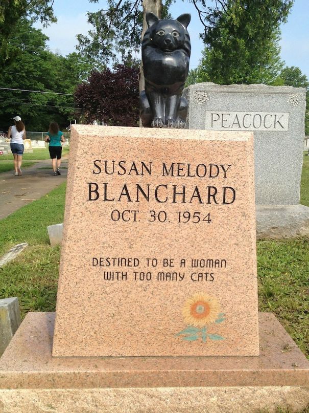 Tombstone with humorous epitaph about having too many cats and a black cat statue on top in a cemetery.