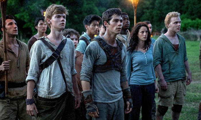 Young cast of The Maze Runner movie standing alert outdoors in a tense scene from popular action movies.