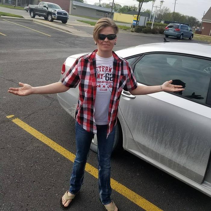 Eric is standing outside near the car with her arms spread Eric is standing outside near the car with her arms spread