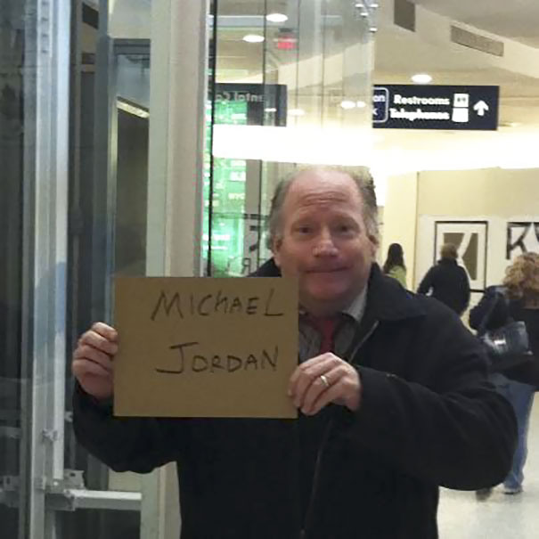 Man holding a funny airport pickup sign that humorously reads "Michael Jordan."