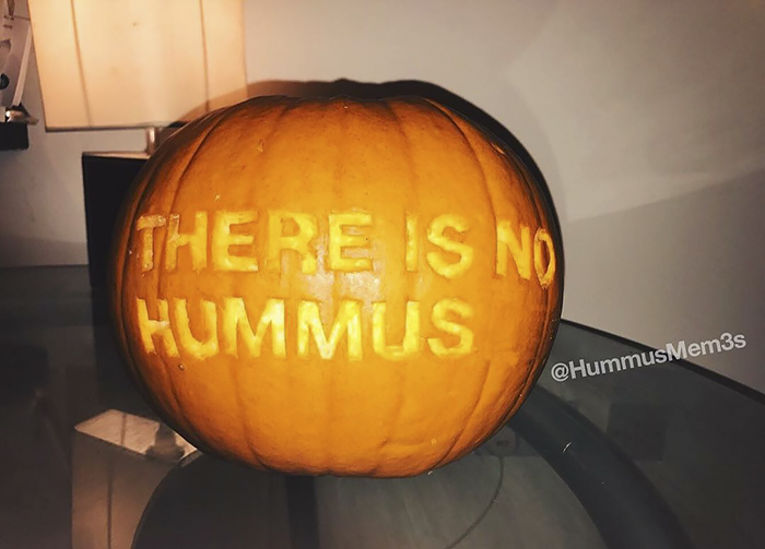 Scary pumpkin carved with "There is no hummus" text on a table indoors.