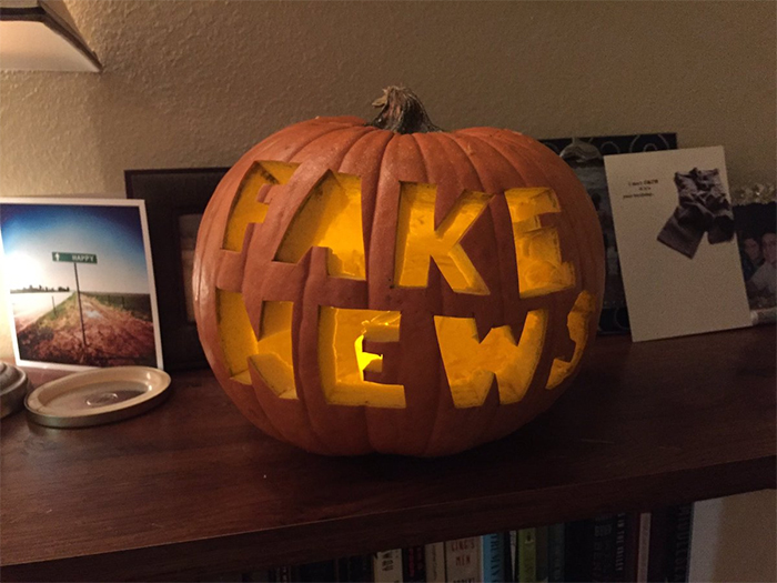 Carved pumpkin with "Fake News" text, illuminated from inside.