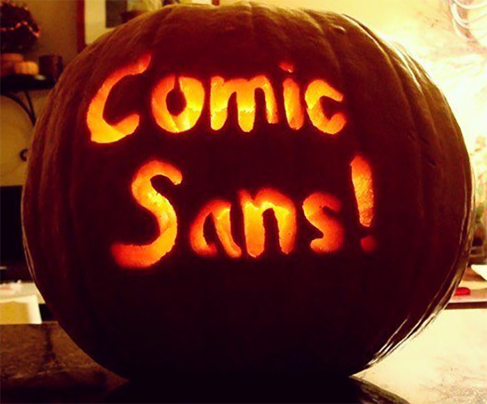 Scary carved pumpkin displaying the words "Comic Sans!" illuminated from within.