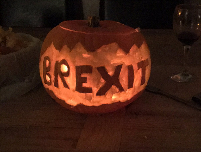 Scary pumpkin carved with the word "Brexit" glowing in dim light on a table.