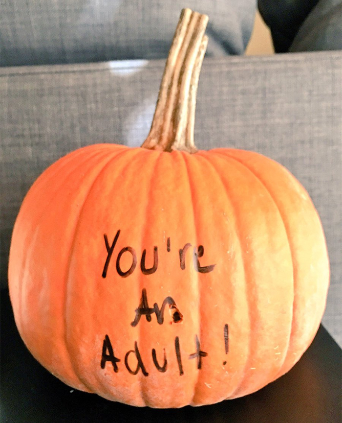 Scary pumpkin with "You're An Adult!" carved into it on a dark background.