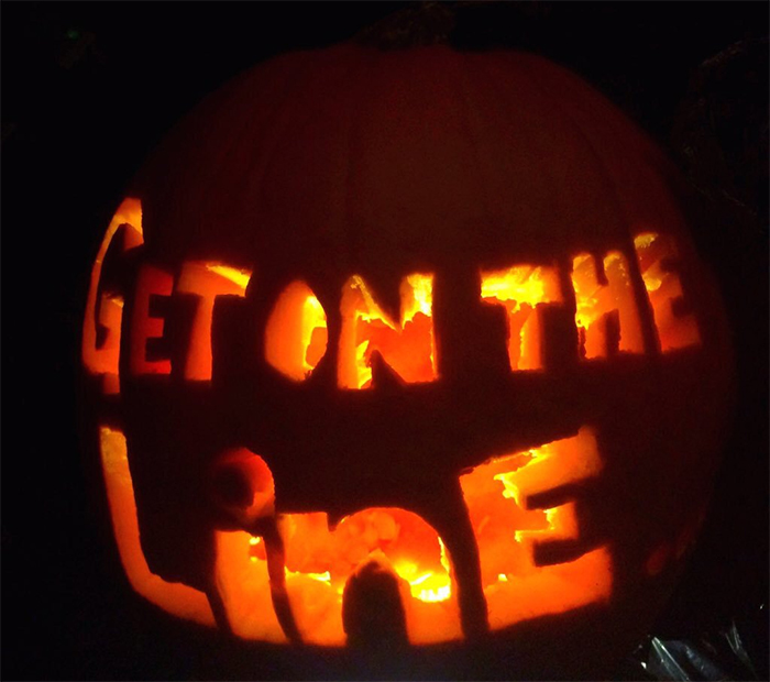 Scary pumpkin carving with words "Get on the Line" glowing in the dark.