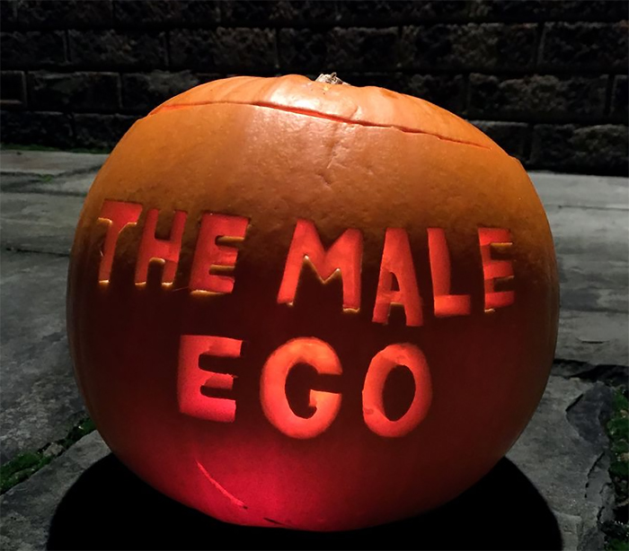 Carved pumpkin with "The Male Ego" text, glowing from within.