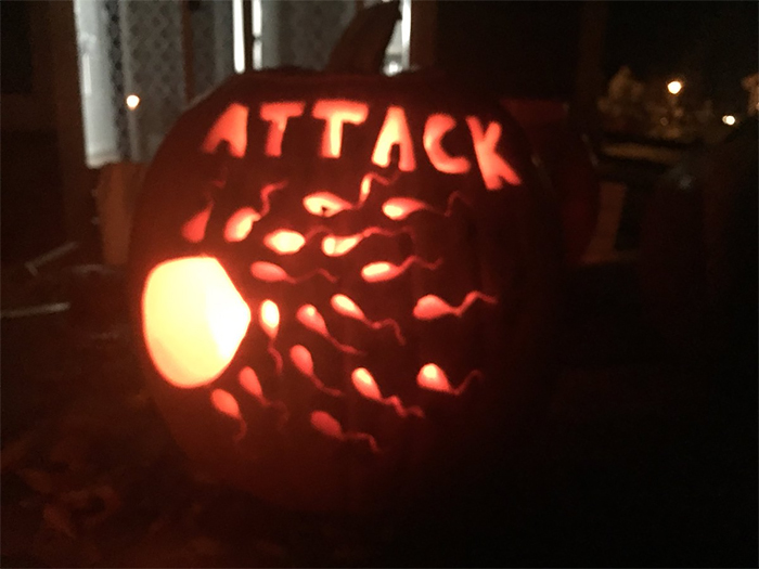 Scary pumpkin carved with "ATTACK" and glowing design reminiscent of swimming shapes, illuminated in the dark.