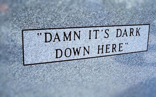 Funny tombstone engraving reading D**n it’s dark down here on a gray granite grave marker with undying humor.