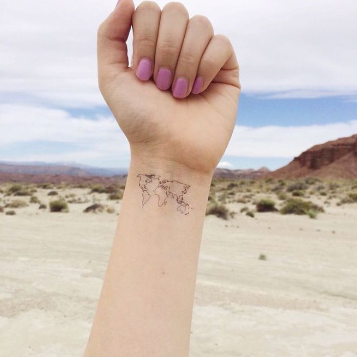 Minimalist travel tattoo of a world map on a wrist, set against a desert landscape.