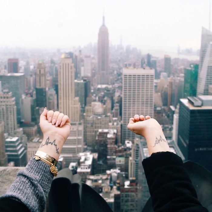 Hands with travel tattoos raised against a cityscape backdrop.