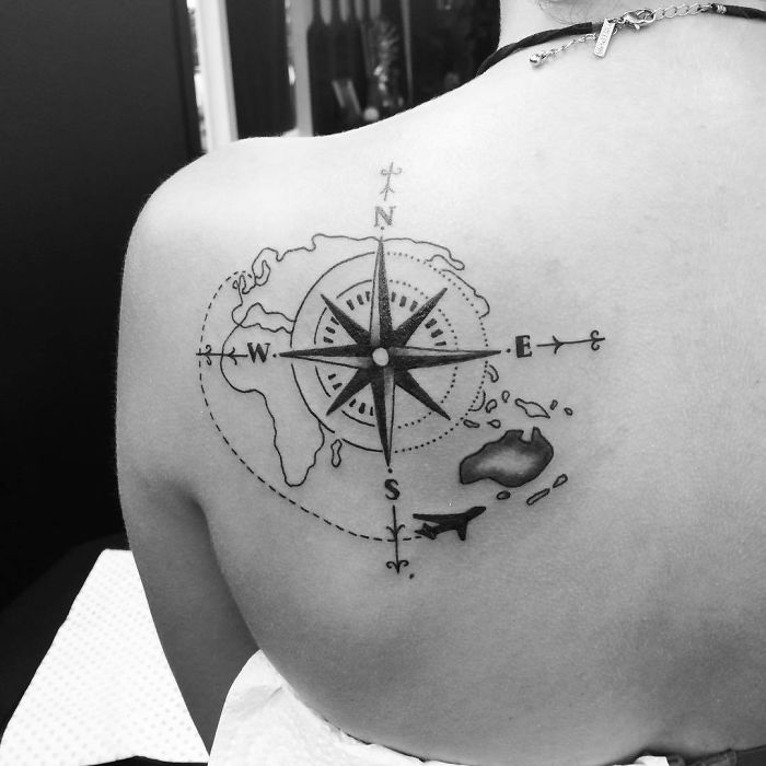 Compass tattoo featuring a world map and plane, symbolizing travel inspiration on a person's shoulder.