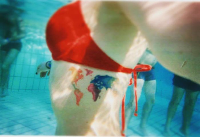 Underwater view of a world map tattoo on a thigh, embodying travel inspiration.