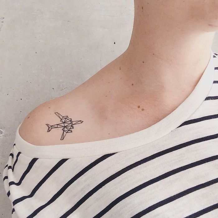Minimal airplane travel tattoo on shoulder, symbolizing wanderlust and adventure, with a striped shirt visible.