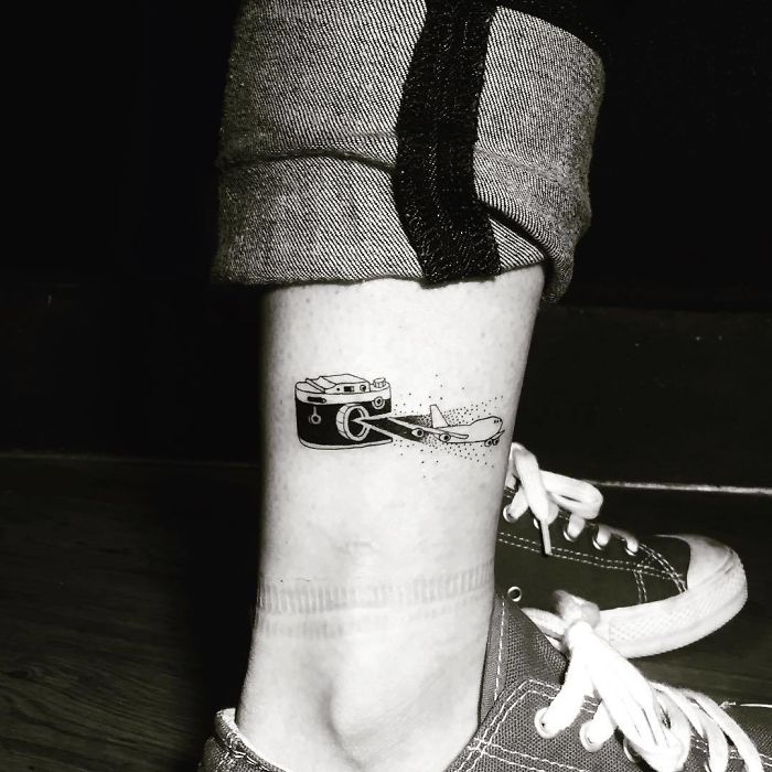 Travel tattoo of a camera and airplane on a person's ankle, symbolizing adventure and exploration.